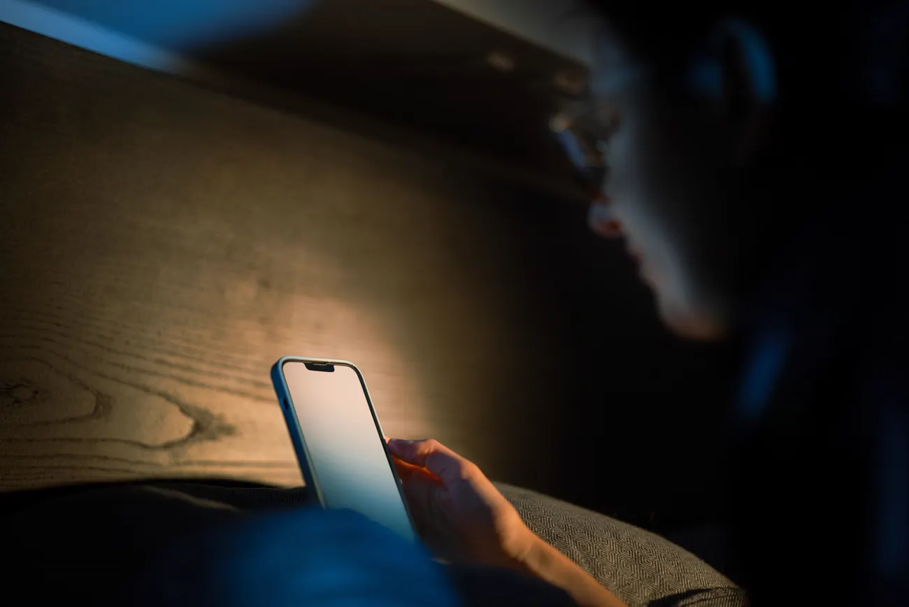 A person lying in the dark, lit by the screen of a phone