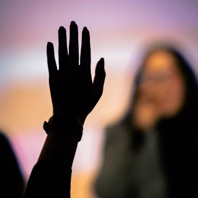 A raised hand silhouetted against a lit screen, waiting to ask a question