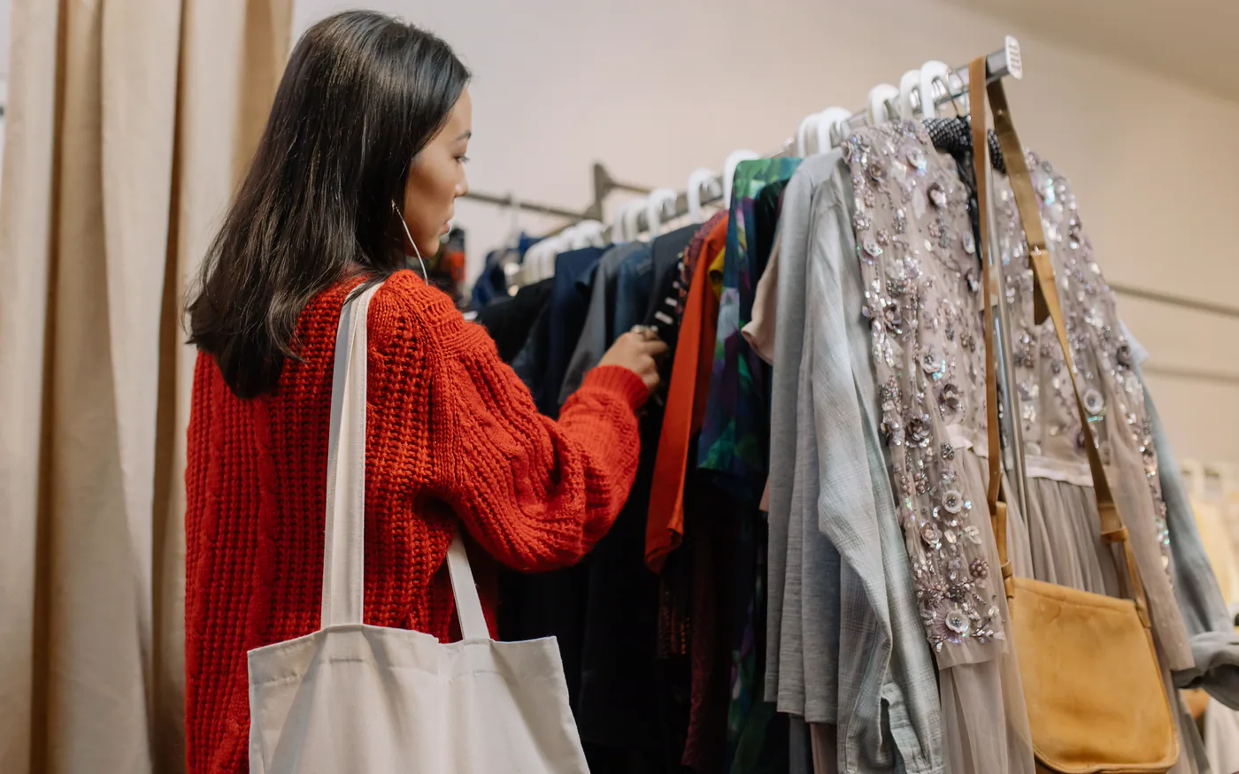 A shopper browsing a clothing rail with a tote bag over one shoulder