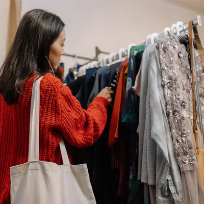 A shopper browsing a clothing rail with a tote bag over one shoulder