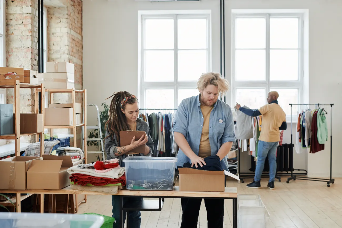 Three store employees unpacking, checking and hanging new clothing stock