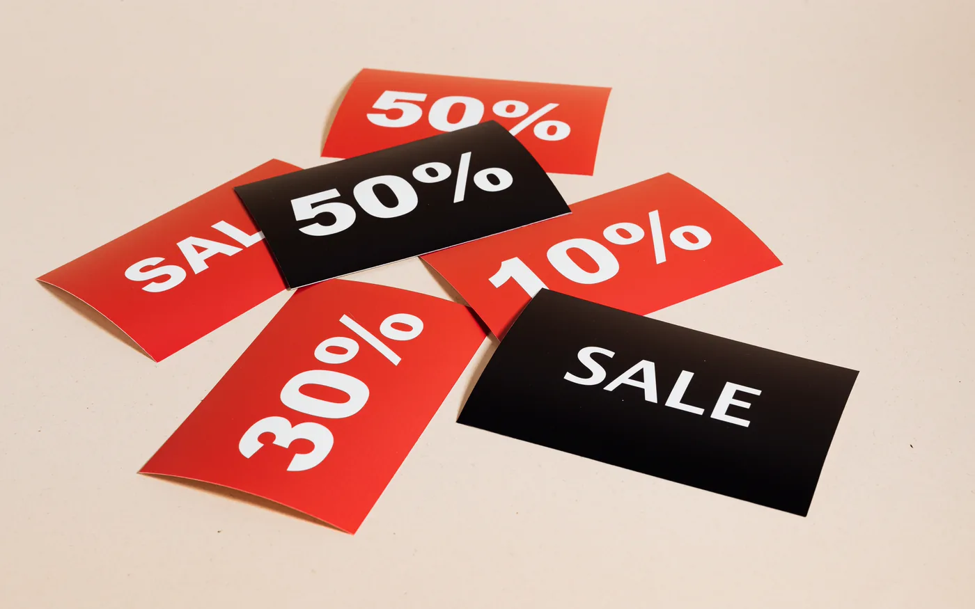 Red and black sale cards marked 10%, 30% and 50% scattered on a beige surface