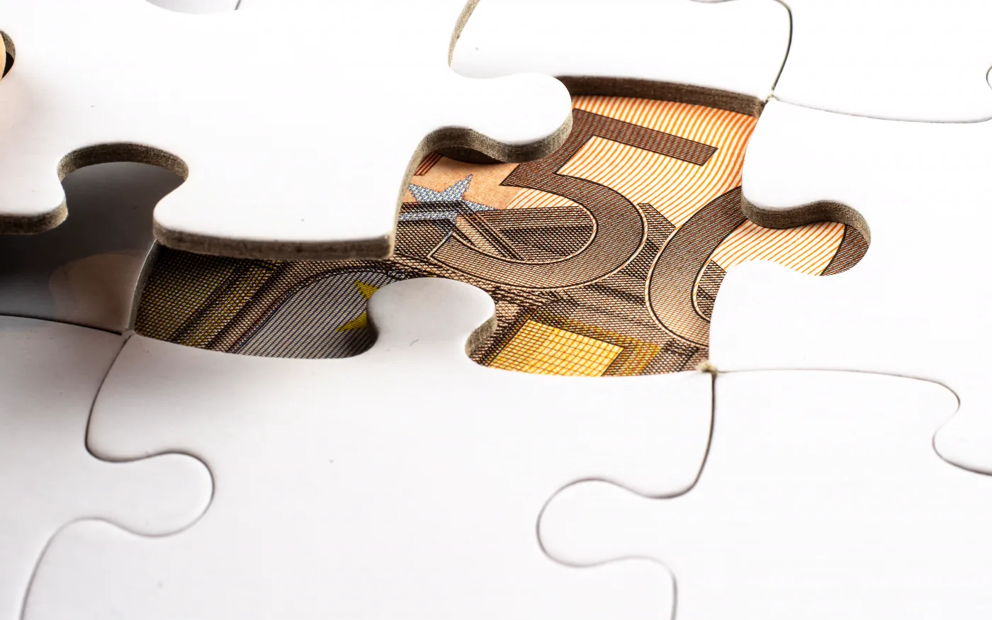 A jigsaw with a missing piece revealing a banknote underneath