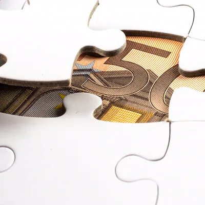 A jigsaw with a missing piece revealing a banknote underneath