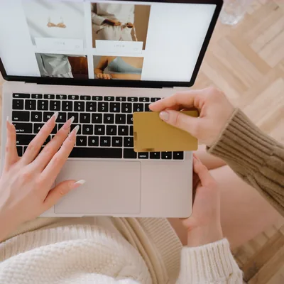A shopper holding a bank card while browsing a store on a laptop