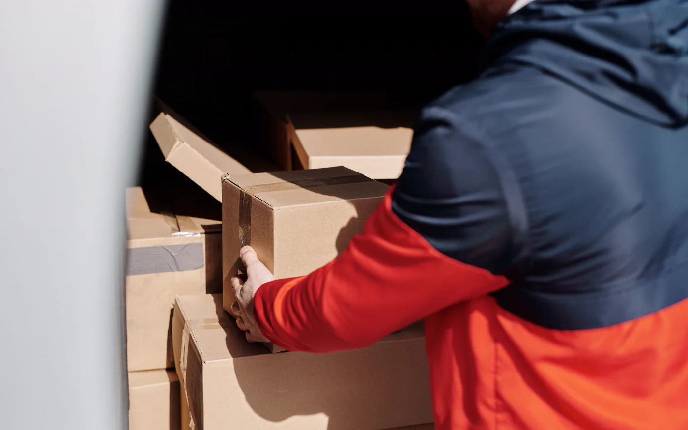 A courier stacking sealed cardboard parcels into a delivery van